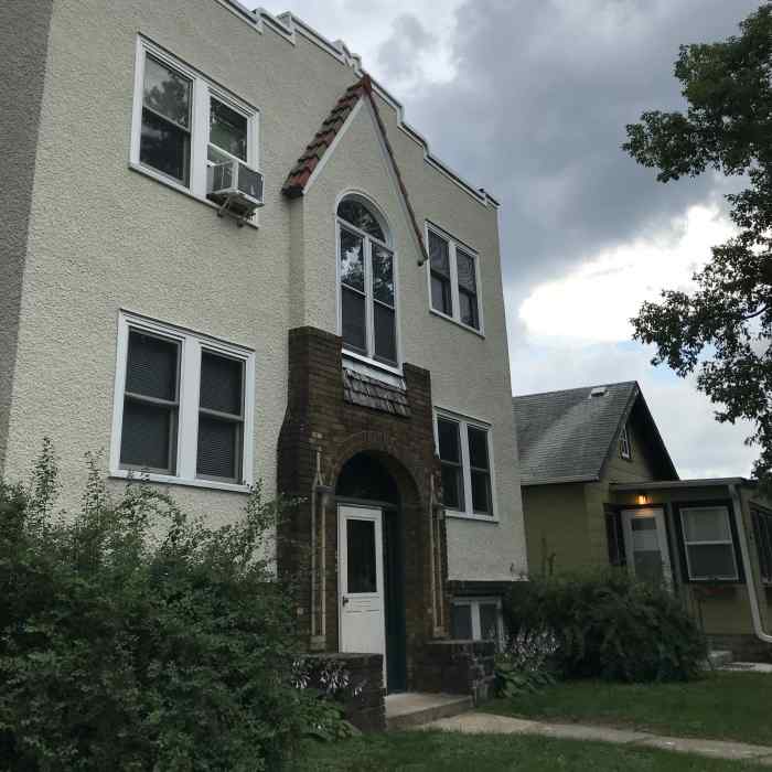 A residential street with a white stucco two-story apartment building at the foreground.