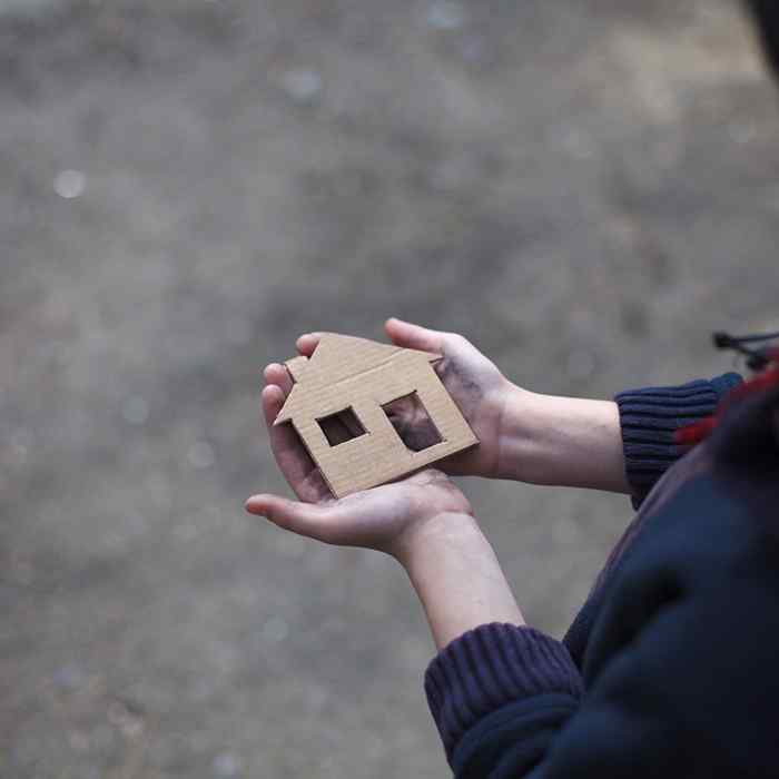 A close-up of a pair of hands holding a cardboard cutout our of house. 