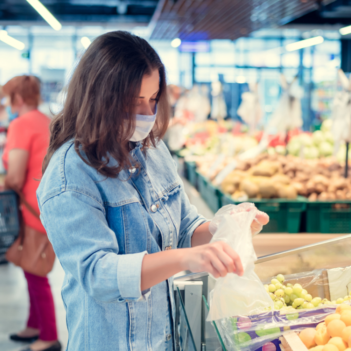 A woman adds fruit to a bag in a grocery store.