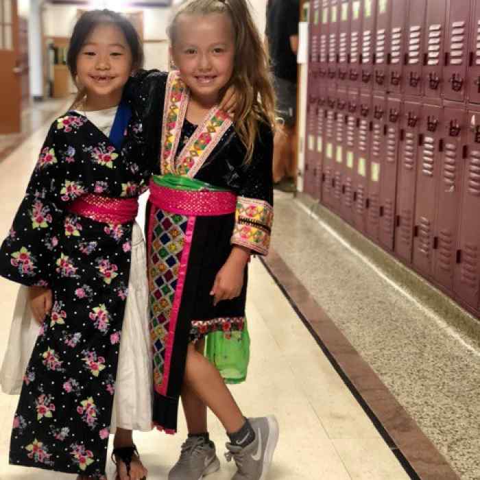 Two girls stand next to each other along a row of lockers.