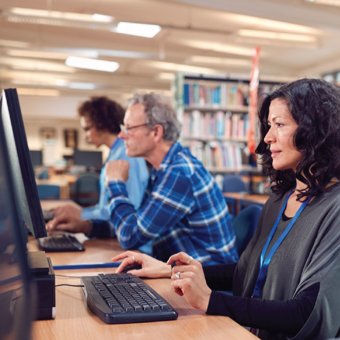 Three people sit next to one another at public library computers.