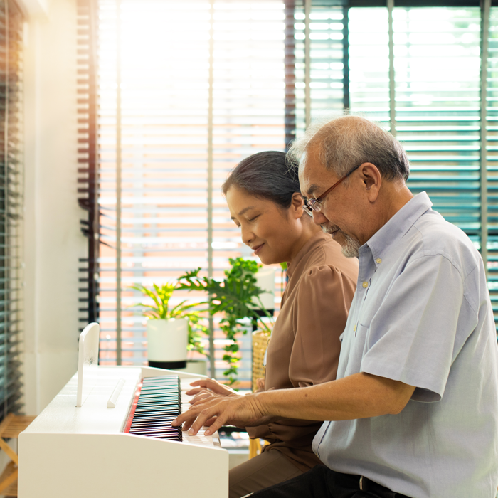 An older adult couple play piano together.