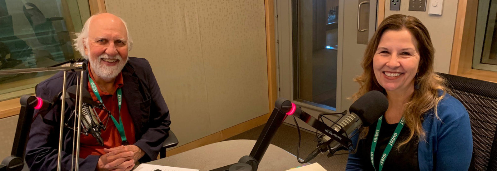 Two adults sit at microphones in a radio booth.