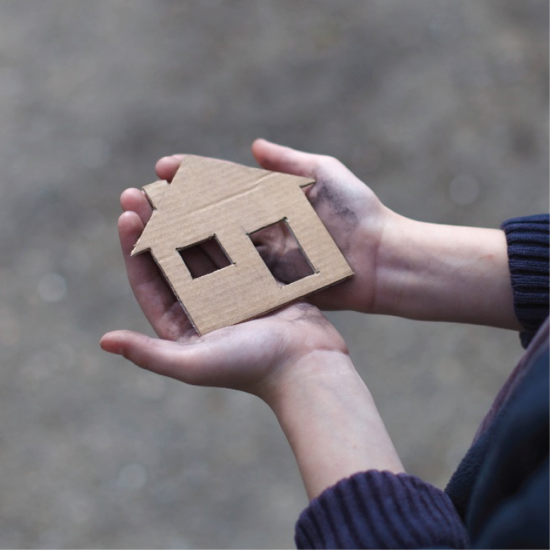 A pair of hands hold a cardboard cutout of a house.