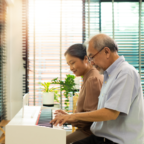 An older adult couple play piano together.