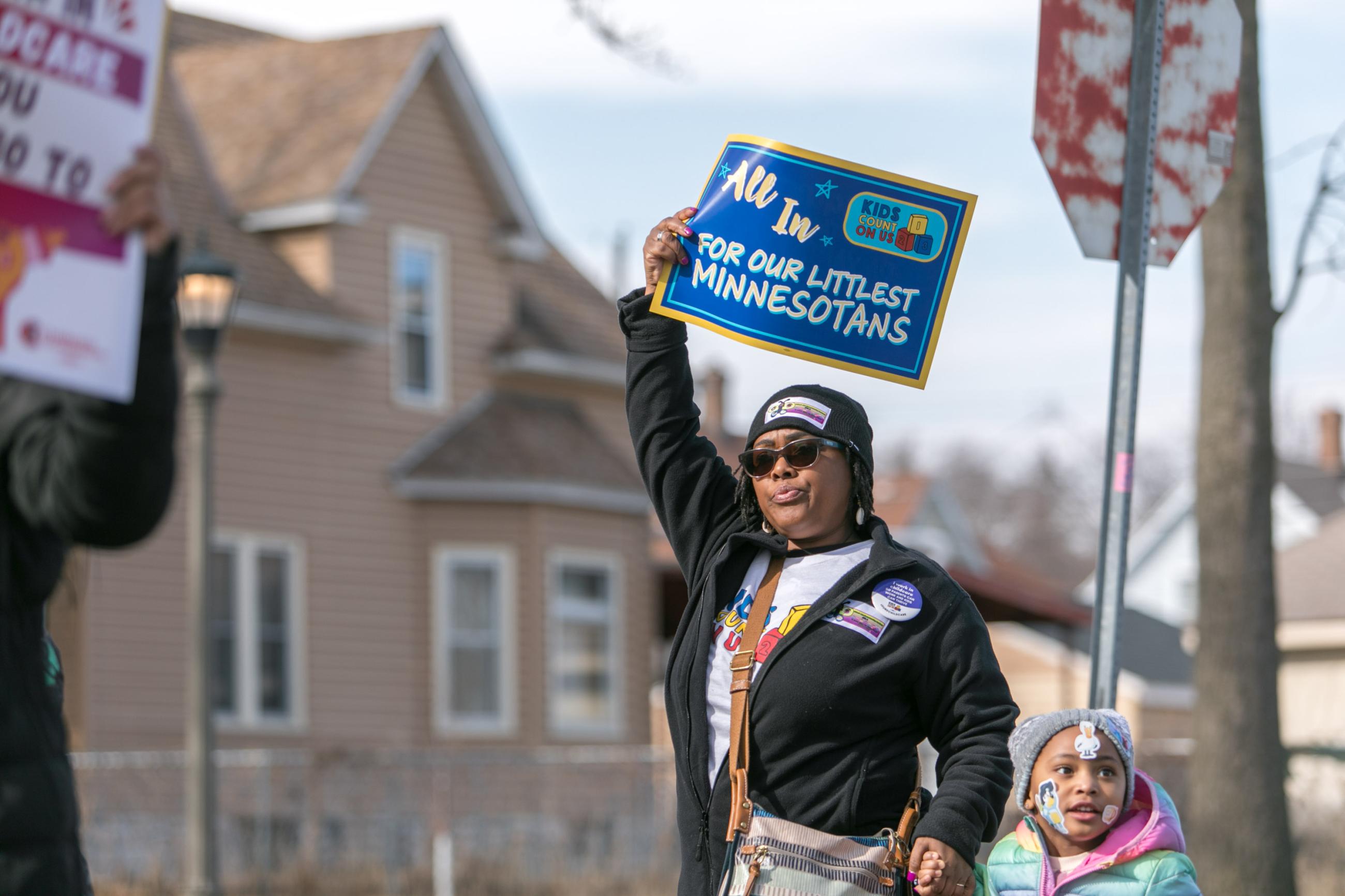 Parent holding up "All In For Our Littlest Minnesotans" sign