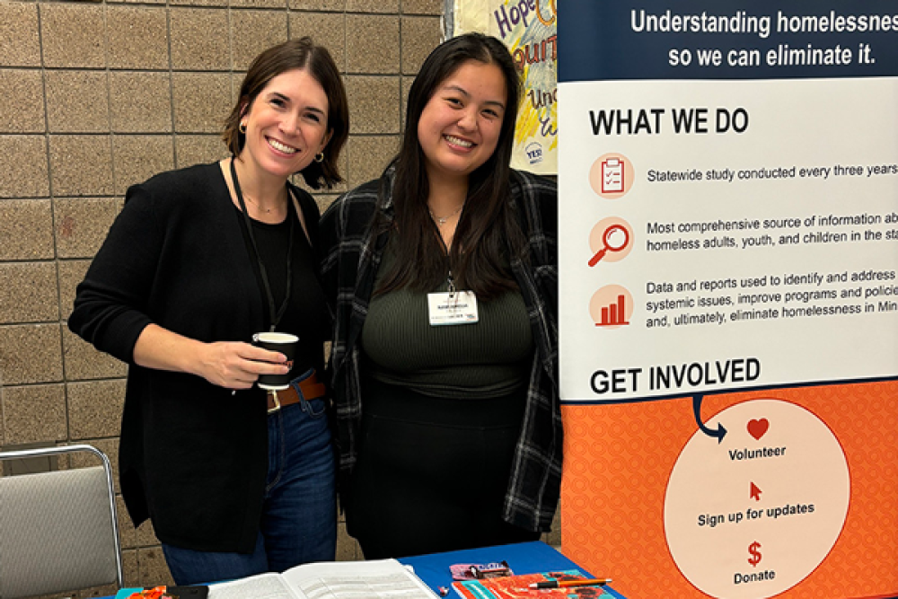 Two women stand at a conference exhibit table ready to answer questions about the Minnesota Homeless Study.