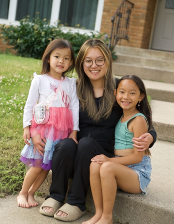 woman and two girls sitting together with house in the background