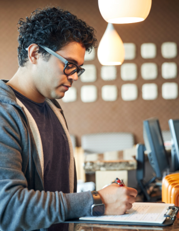 A person fills stands at an office counter filling out a form.