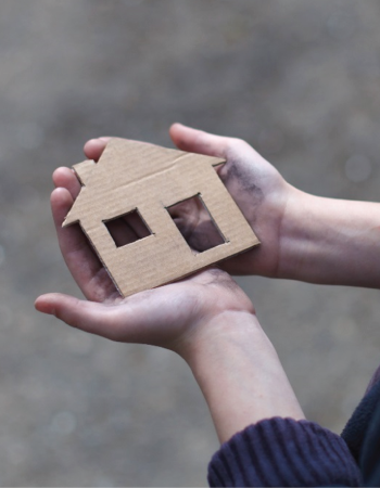 A pair of hands hold a cardboard cutout of a house.