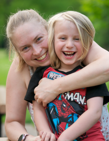 Photo of a mom hugging child, both smiling and looking at the camera